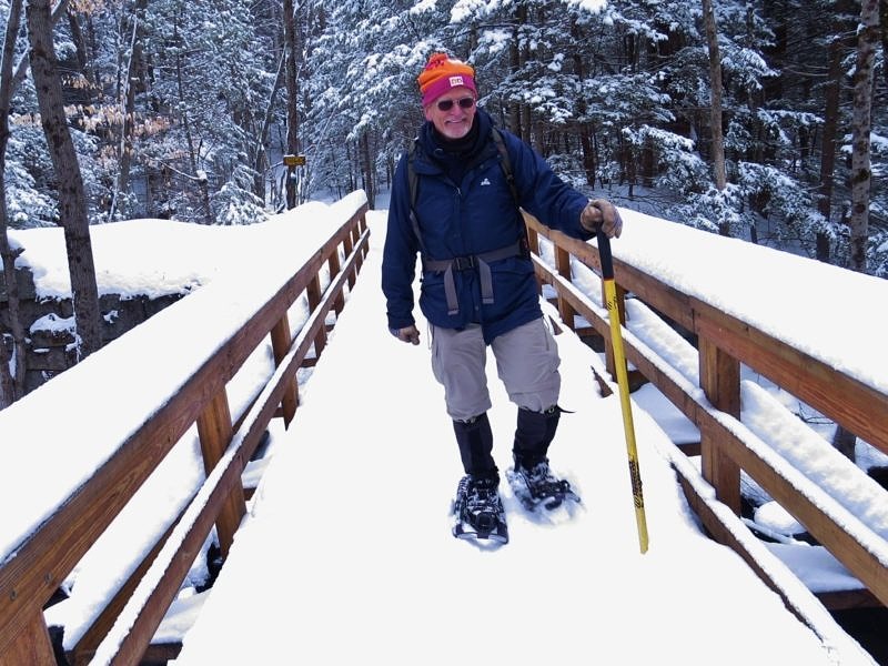 A happy hiker snowshoes on the footbridge over Nubanusit Brook, on the Eastview Trail. (photo © Meade Cadot)