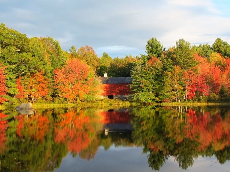 A red barn surrounded by fall foliage and reflected in Merrills Pond, Hancock, NH. (photo © Brett Amy Thelen)