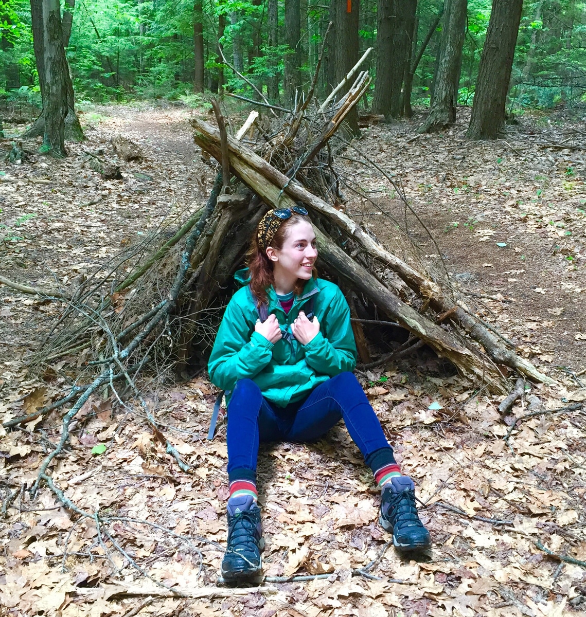 Shauna Sousa sits "in" a woodland fort on the Harris Center's Hiroshi Loop Trail.
