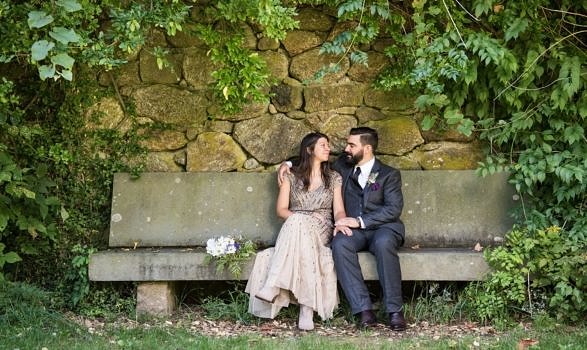A bride and groom sit together on a stone bench, tucked away in a corner of the Harris Center grounds. (photo © Brown-Hawk Family via the Flickr Creative Commons license)