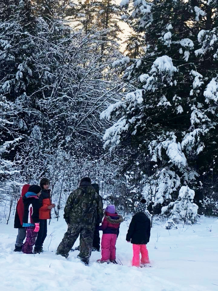 A group of kids gather together in snowy woods.