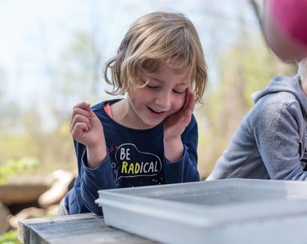 A preschooler smiles while taking a close look at a worm on a Harris Center-led outing. (photo © Ben Conant)