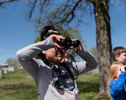 A 3rd grader peers through binoculars during a birding outing in Keene with Harris Center teacher-naturalist Polly Pattison. (photo © Ben Conant)