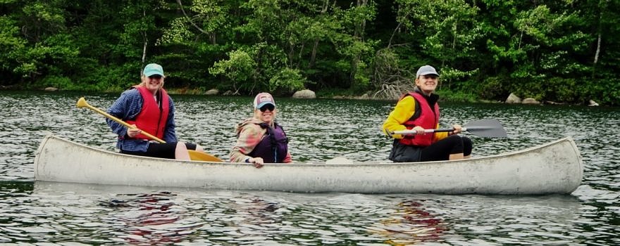 KSC conservation interns Lauren Peyser (left) and Audrey Kaiser (right) paddle with KSC faculty supervisor Karen Seaver (middle) to Harris Center-protected land on the shoreline of Nubanusit Lake. Note the smiles -- this photo was taken before discovering the dead eagle chicks!