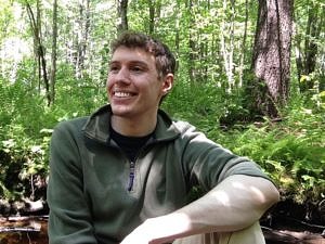 Harris Center intern Matt Harrison sits and smiles in the woods.