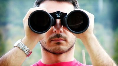 A young man peers through binoculars. (photo © gerlos via the Flickr Creative Commons)