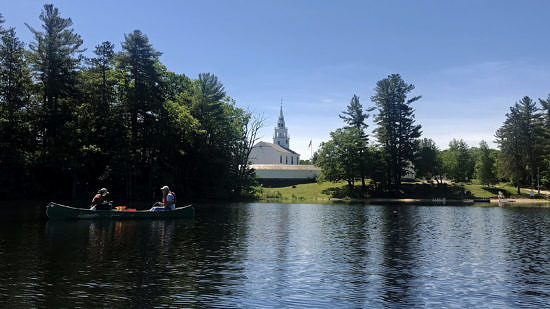 A canoe floats on Norway Pond in Hancock, with the town church and barn in the background. (photo © Brett Amy Thelen)