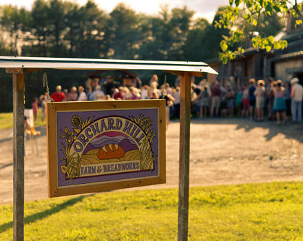 A photo of the "Orchard Hill Breadworks" sign, with people lining up in the background for pizza. (photo © Chad Cassin)