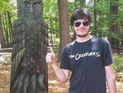 Tristan Hayes smiles in front of a carved wooden owl.