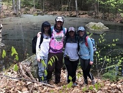 Four college students pose in front of a vernal pool.