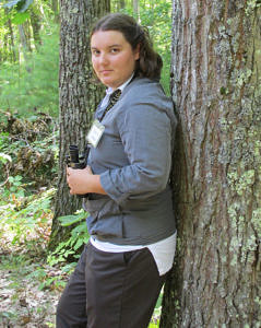 Kim Snyder leaning against a tree, holding binoculars.
