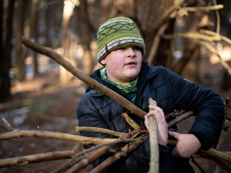 A middle school boy gathers sticks to build a shelter in the woods. (photo © Ben Conant)