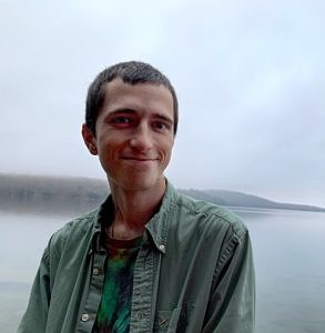 Alec Kaisand smiles while standing at the edge of a lake.