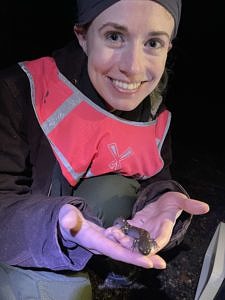 A woman in a bright pink vest smiles while holding a spotted salamander in their hands. (photo © Meg Hussey)