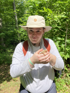 A young man in a tan brimmed hat and gray shirt holds a toad in his hands.