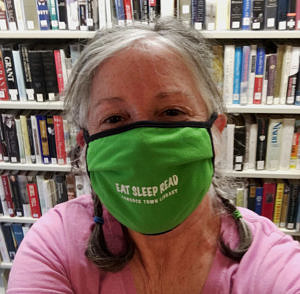 Hancock Town Library Director Amy Markus, wearing a green face mask and sitting in front of library bookshelves.