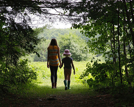 Two girls walk hand in hand from the woods into the field at the Fremont Conservation Land in Peterborough. (photo © Francie Von Mertens)