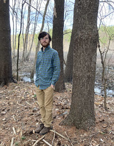 Daniel Medeiros stands in front of a tree at the edge of a wetland. (photo © Daniel Medeiros)