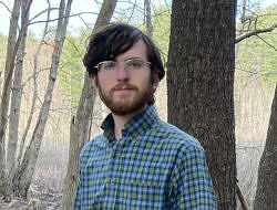 Daniel Medeiros standing in front of a tree, wearing glasses and a blue checkered shirt.