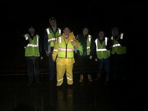 A group of young adults stand on a wet street in raingear and reflective vests. (photo © Karen Seaver)