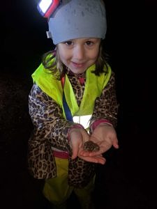 A young girl in a reflective vest holds a wood frog in her hands. (photo © Gabe Roxby)