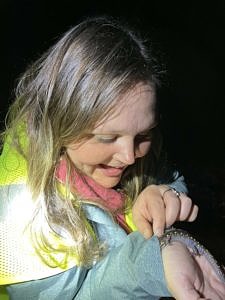 A young woman smiles while looking down at a salamander that is crawling on her rain jacket. (photo © Karen Seaver)