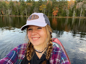 Mallory Roof smiles from the seat of a kayak in the middle of New Hampshire pond.