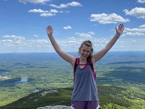 Rachel Ranelli, standing on the summit of Mount Monadnock with her arms in the air on a bluebird day.
