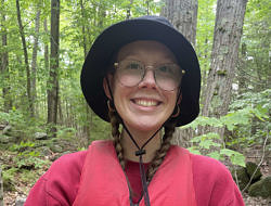 Taylor Jackson smiles while wearing a bucket hat in the forest.