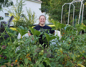 Kara Reynolds stands behind a large tomato plant with her hands on her hips.
