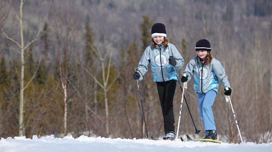 Two children cross-country ski through an open field, with woods in the distance. (photo © Province of British Columbia via the Flickr Creative Commons)