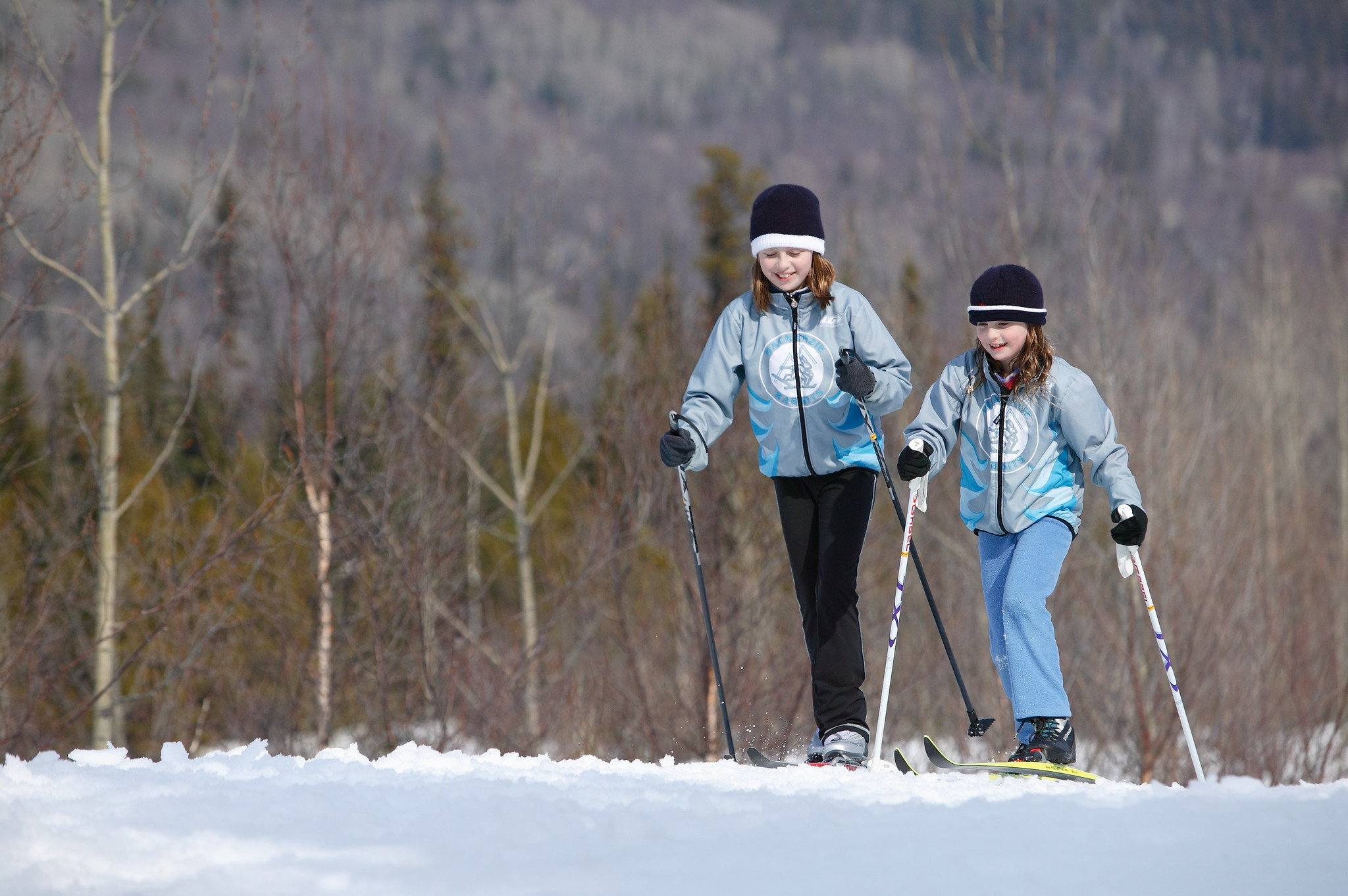 Two children cross-country ski through an open field, with woods in the distance. (photo © Province of British Columbia via the Flickr Creative Commons)