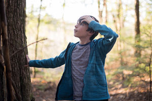 A middle school boy stands in the woods, looking up at a tree in wonder. (photo © Ben Conant)