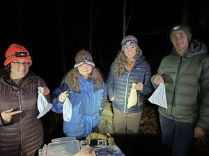Four owl banding staff and volunteers hold cloth bags, each containing a saw-whet owl, on the "big night" of October 27, 2022. (photo © Brett Amy Thelen)
