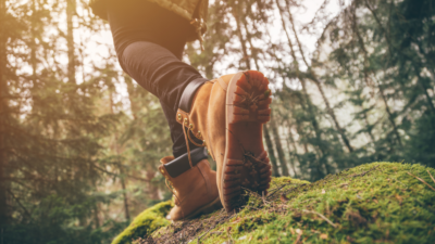 A person wearing black jeans and Timberlands walking on a mossy rock (photo © Canva Commons)