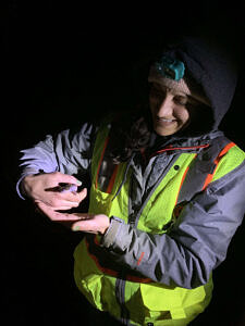 A person smiles while looking down at the spotted salamander they're holding in their hands. (photo © Jenna Rich)