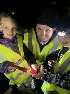 A mother and two children, all clad in reflective vests and carrying flashlights, gather around a spotted salamander that one child is holding in their hand. (photo © Karen Seaver)