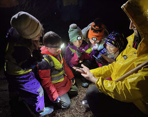 A group of children wearing rain gear and reflective vests gather around an adult, who is holding a spotted salamander in his hand. (photo © Kara Reynolds)