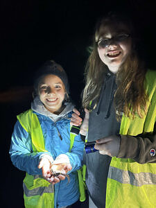 Two kids wearing reflective vests smile while holding a spotted salamander. (photo © Lisa Schroeder) 