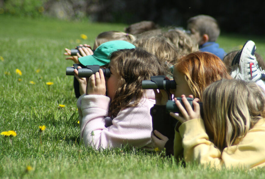 Students lie in the grass, observing through binoculars (photo: Eric Aldrich)