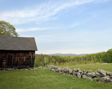 A dark-paneled barn sits in a green field with a stone wall against a blue sky. (photo: Brett Amy Thelen)