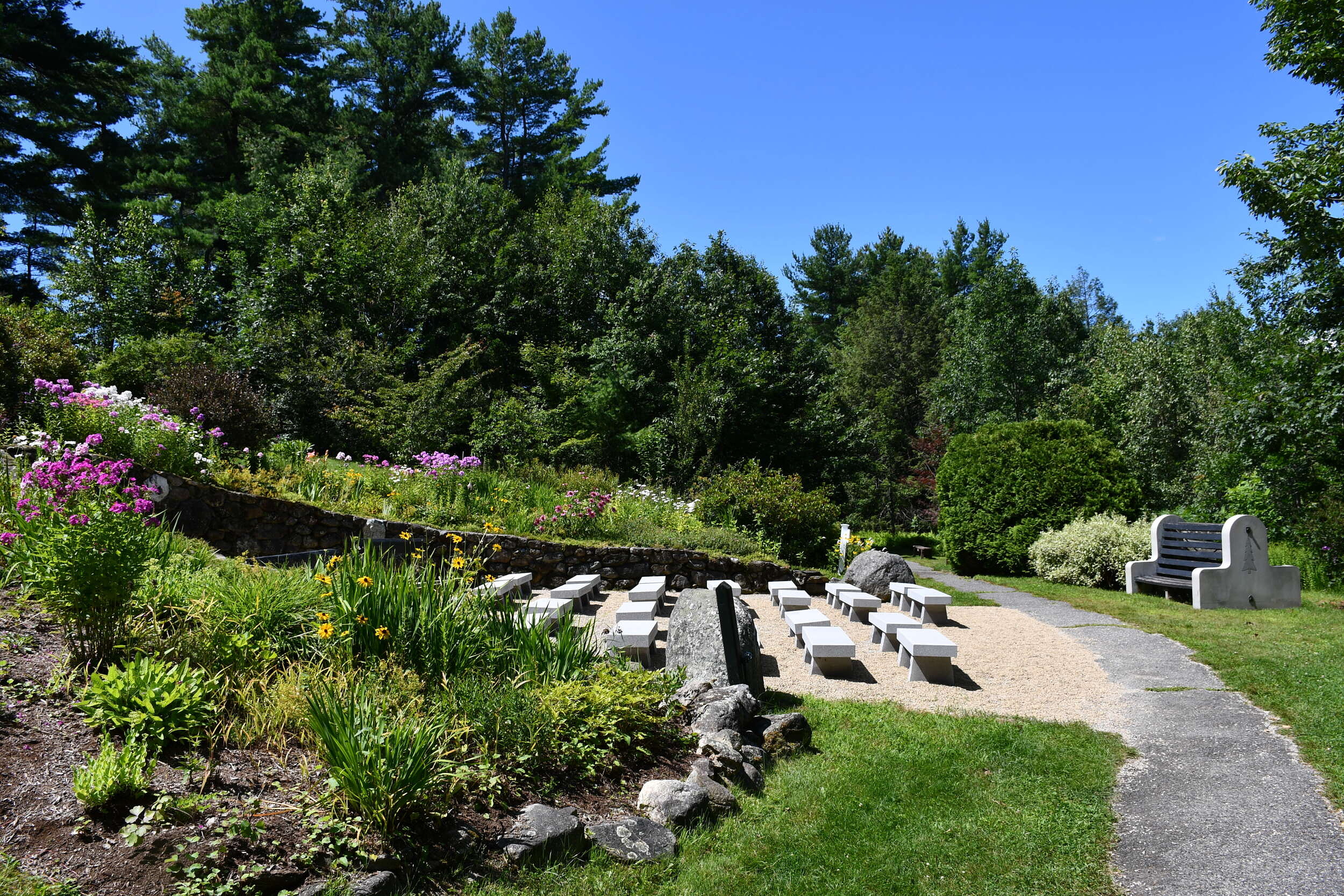 Flowers grow along a small slope, with rows of white benches between, next to a walking path. (photo © Audrey Dunn)