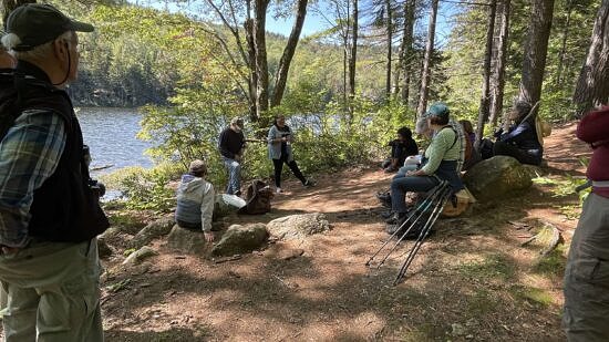 A group of people sit on the edge of Jack's Pond, listening to a speaker. (photo © Susie Spikol)