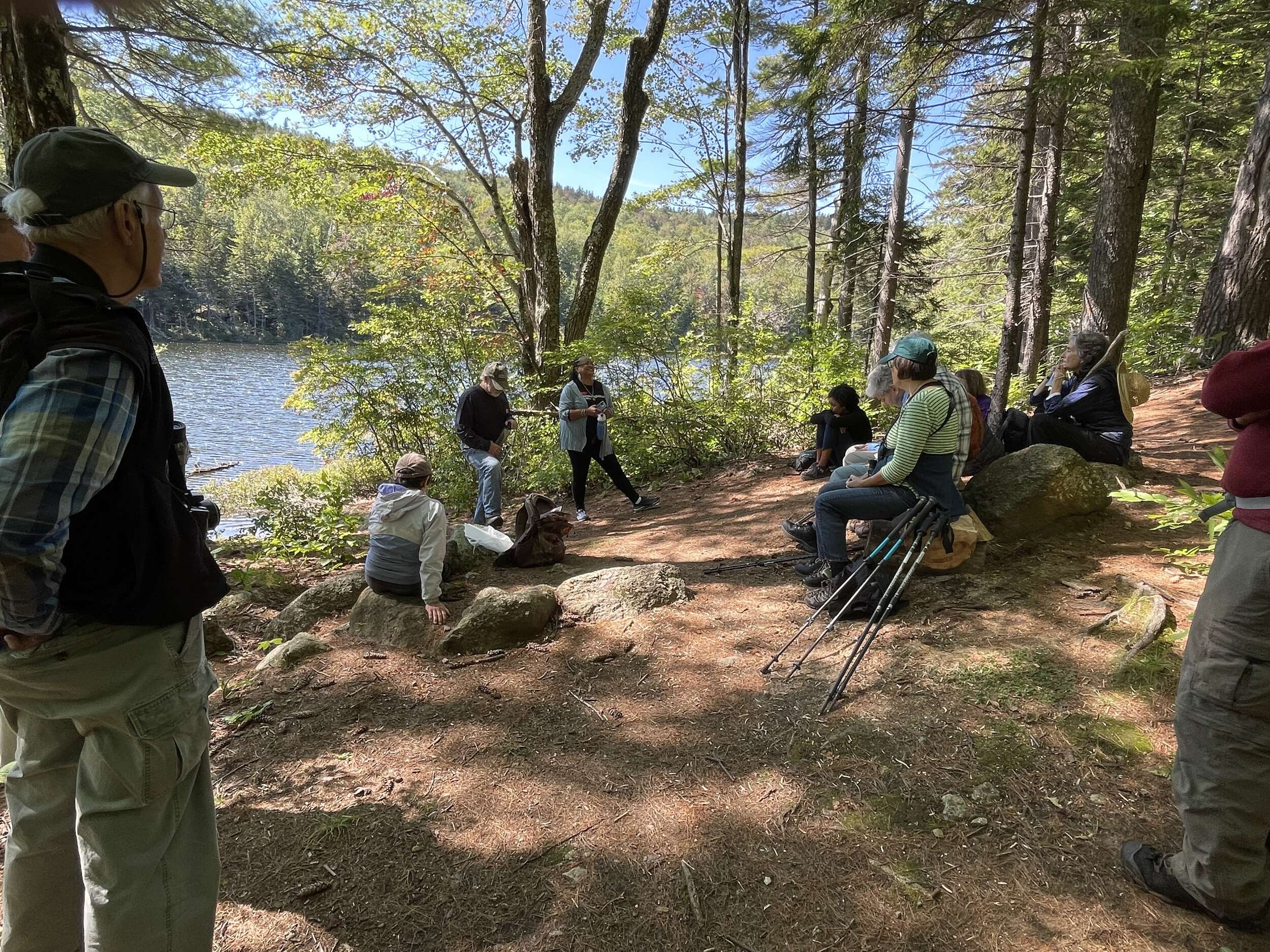 A group of people sit on the edge of Jack's Pond, listening to a speaker. (photo © Susie Spikol)