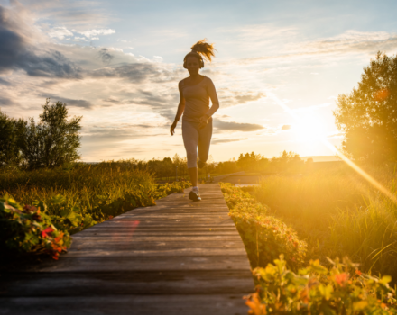 A woman runs down a boardwalk, with the sun setting behind her. (photo © Canva Commons)