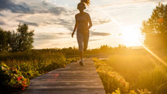 A woman runs down a boardwalk, with the sun setting behind her. (photo © Canva Commons)