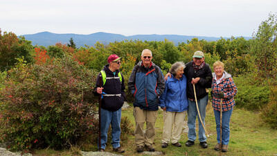 Five people, wearing hiking gear, stand in a line and smile on a mountain top. (photo © Meade Cadot)