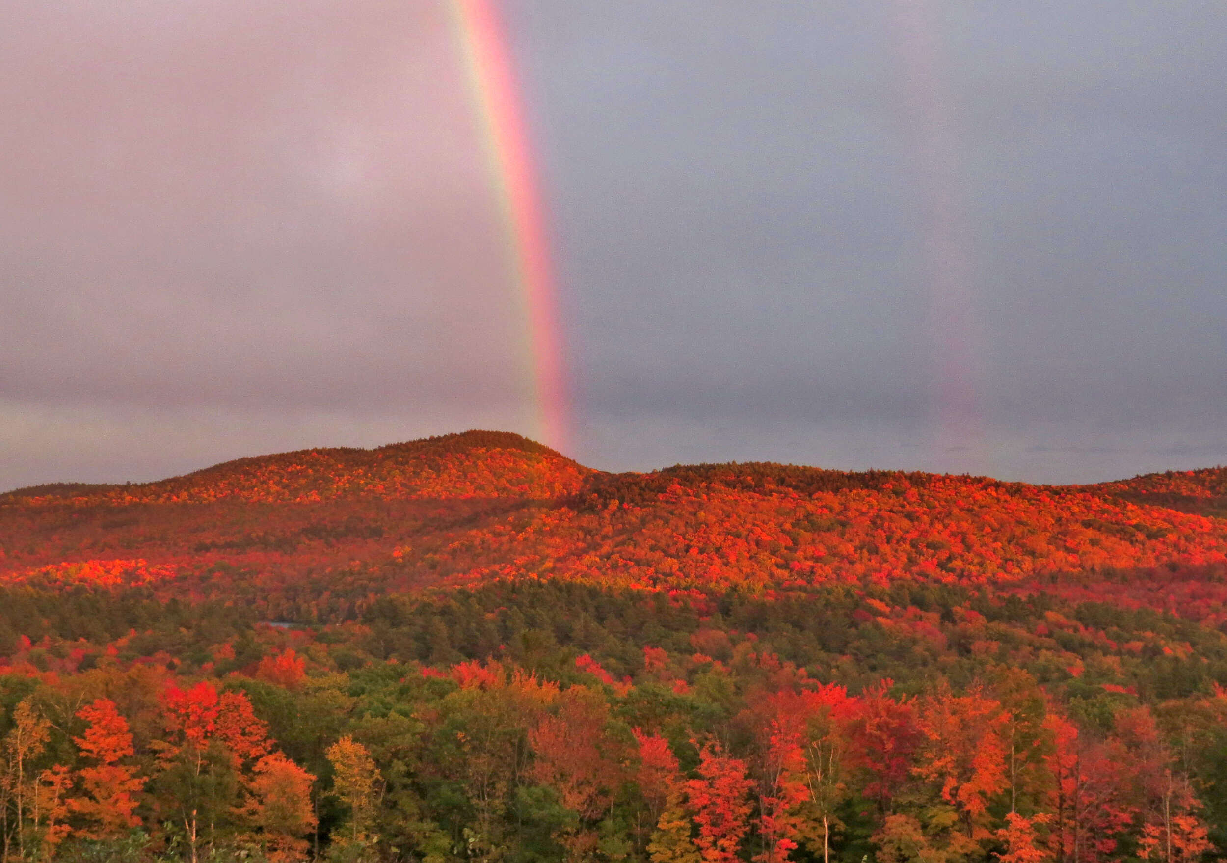 A rainbow ends at Thumb Mountain, red and orange with fall foliage. (photo © Meade Cadot)