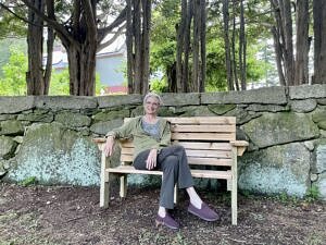 Lisa Murray sits on a newly installed wooden bench under some yew trees. (photo © Audrey Dunn)
