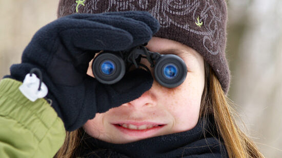 A girl, dressed for winter, looks through binoculars. (photo © Eric Begin)